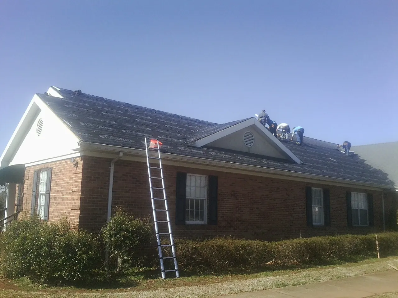 Crew tearing shingles off a brick ranch roof with a ladder set — Metal Roof Repair work by our crew in Antioch